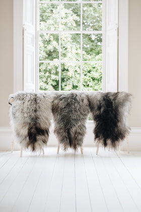 3 sheepskin rugs draped on back of  chairs infront of window