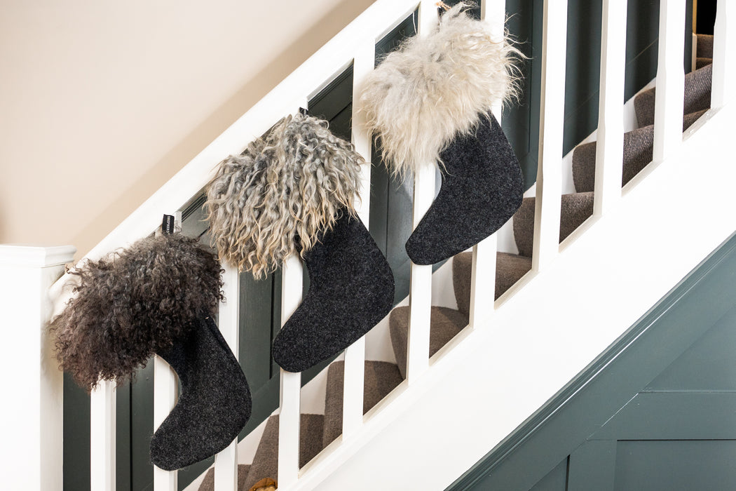 Gotland Sheepskin and wool Christmas Stockings. Three Gotland Sheepskin Cuffed wool stockings displayed on a banister rail. Gotland Sheepskins varies in colours, each stocking being greys, cream and white. The foot of the stocking is a wool material.