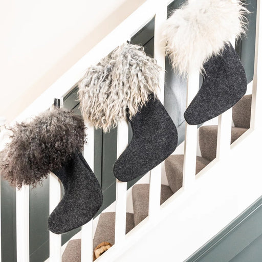 Gotland Sheepskin and wool Christmas Stockings. Three Gotland Sheepskin Cuffed wool stockings displayed on a banister rail. Gotland Sheepskins varies in colours, each stocking being greys, cream and white. The foot of the stocking is a wool material.